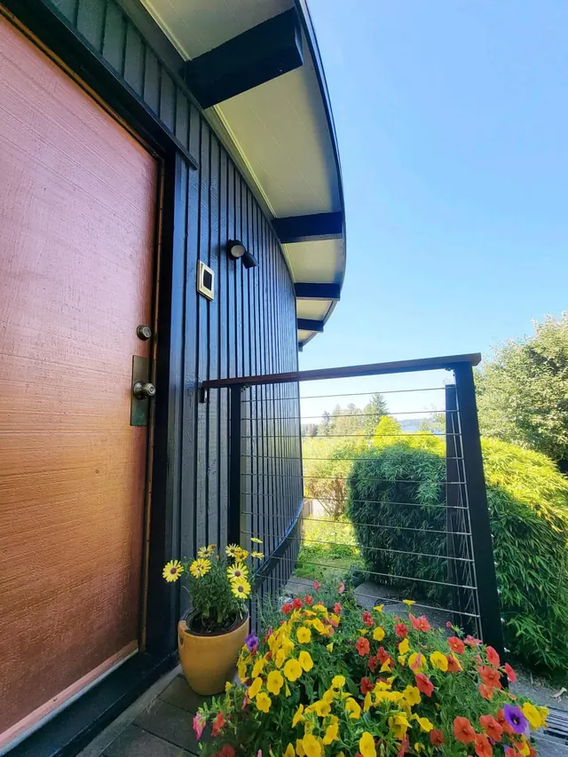 Freshly painted charcoal siding and soffit beside a wood front door and flower planters