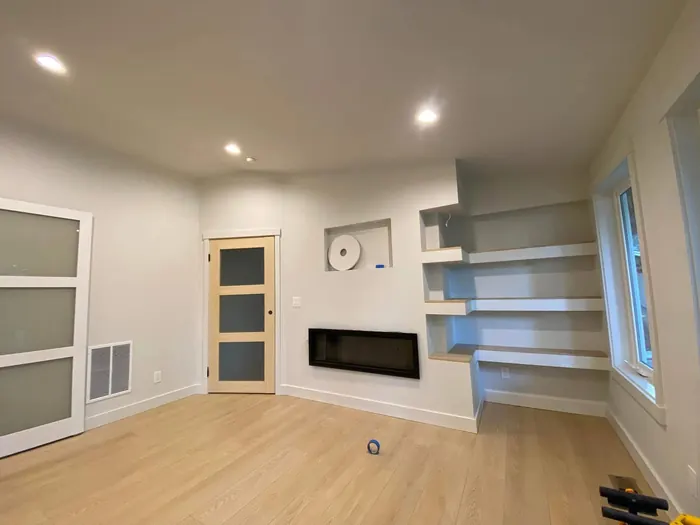 Finished room with smooth white walls, painted floating shelves and a linear fireplace
