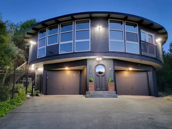 Round house after: deep charcoal siding with crisp white window frames, lit at dusk
